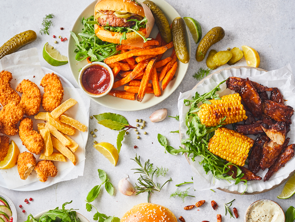 Plant-based retail market overview 2 An aerial view of three plates of plant-based food featuring plant-based breaded chicken, a plant-based burger, french fries, and corn on the cob